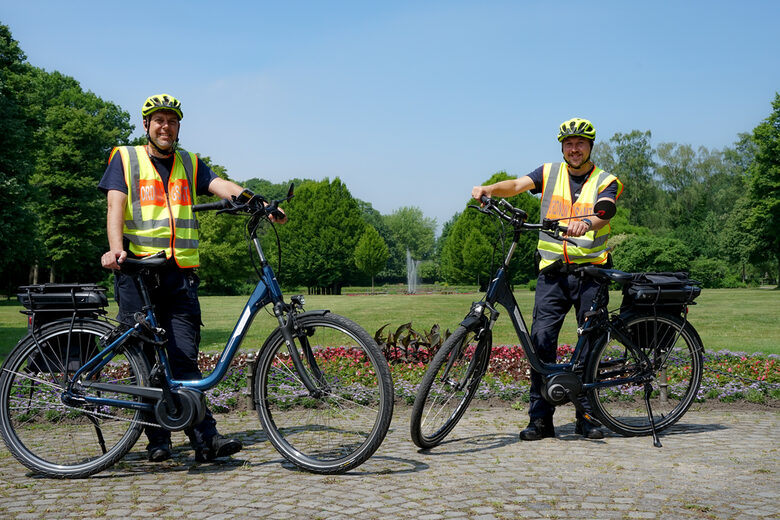 Zwei Mitarbeiter vom KOD stehen im Stadtgarten hinter ihren E-Bikes
