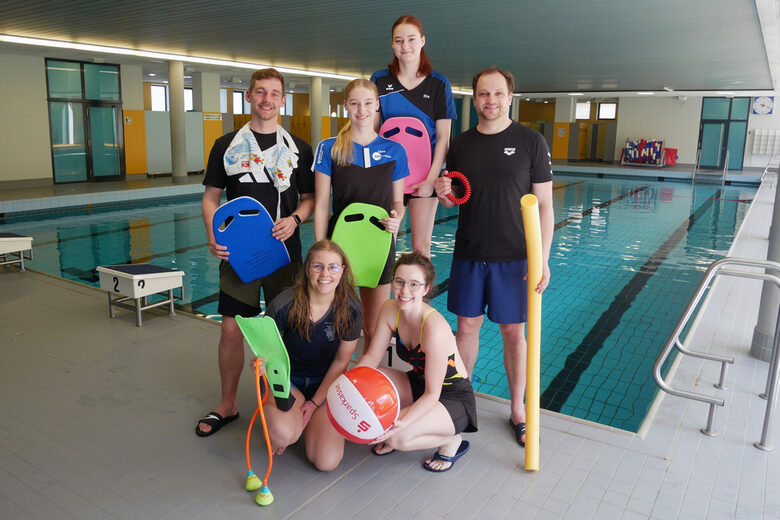 Gruppenfoto Trainer vor Schwimmbecken mit Schwimmutensilien
