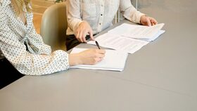 Zwei Frauen sitzen an einem Tisch und unterschreiben Dokumente